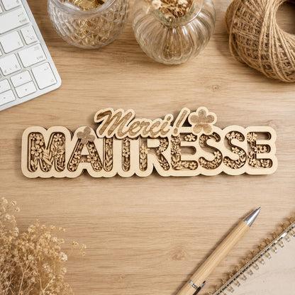 Décoration en bois multicouches L'Atelier de Lylou avec le texte "Merci Maitresse" et des motifs floraux gravés. Idée cadeau maîtresse.