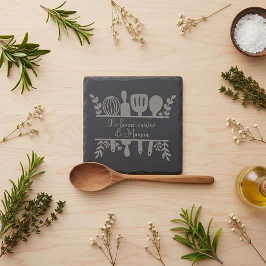 Dessous de plat carré en ardoise naturelle noire, gravé "La bonne cuisine de Maman" avec des ustensiles de cuisine. L'Atelier de Lylou.
