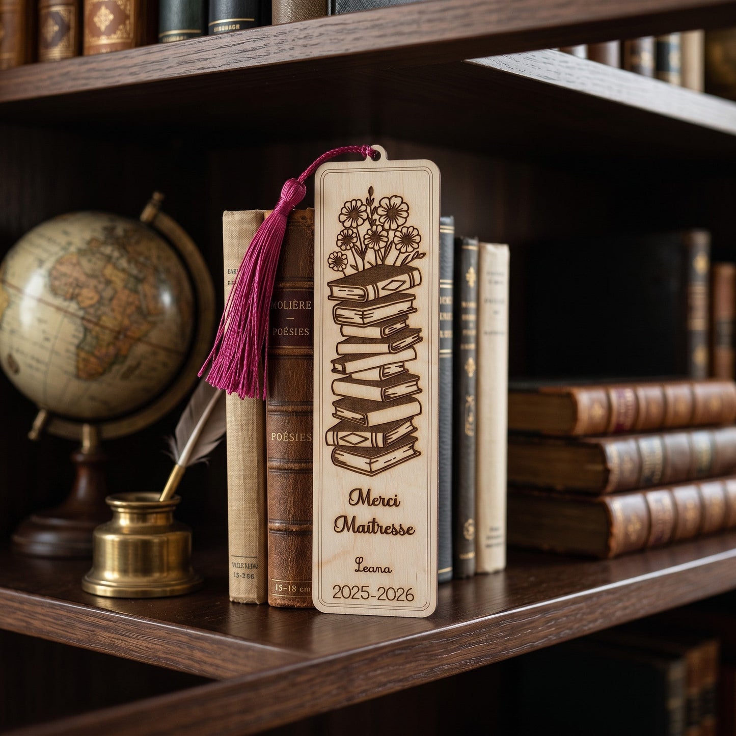 Marque-page personnalisé en bois L'Atelier de Lylou, gravé d'une pile de livres et de fleurs, avec le texte "Merci Maîtresse Leana 2025-2026" et un pompon fuchsia.