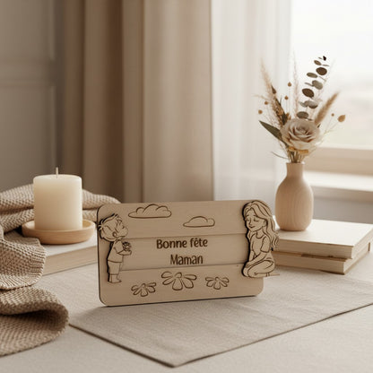 Plaque en bois L'Atelier de Lylou "Bonne fête Maman" avec un garçon offrant des fleurs et une fille assise, décorée de nuages et de fleurs.