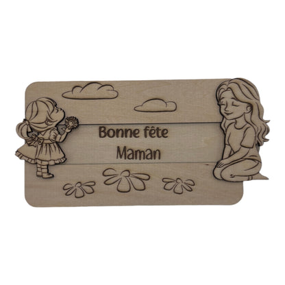 Plaque en bois "Bonne fête Maman" de L'Atelier de Lylou, avec une petite fille offrant une fleur et une femme assise, décorée de nuages et de marguerites.
