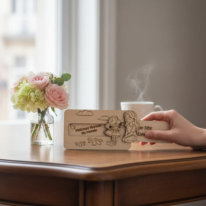 Plaque en bois L'Atelier de Lylou gravée d'une mère et d'une fille s'offrant des fleurs. Texte : Meilleure Maman du monde, Bonne fête Maman.